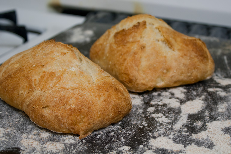 French rolls with a thick, crunchy crust, resting on a floured baking sheet.
