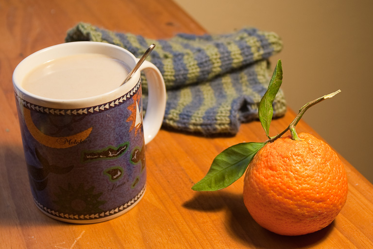 A satsuma mandarin orange and a cup of coffee. Fingerless mitts in the background.